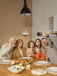 A family with three generations takes a selfie at a dinner table with roast chicken.