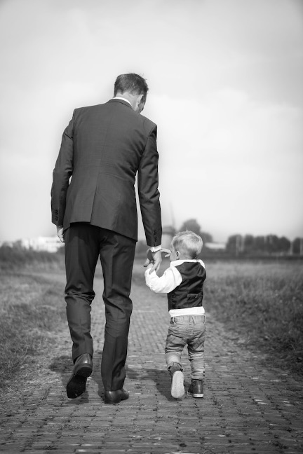 Father and young son hold hands while wearing suits and walking outdoors.